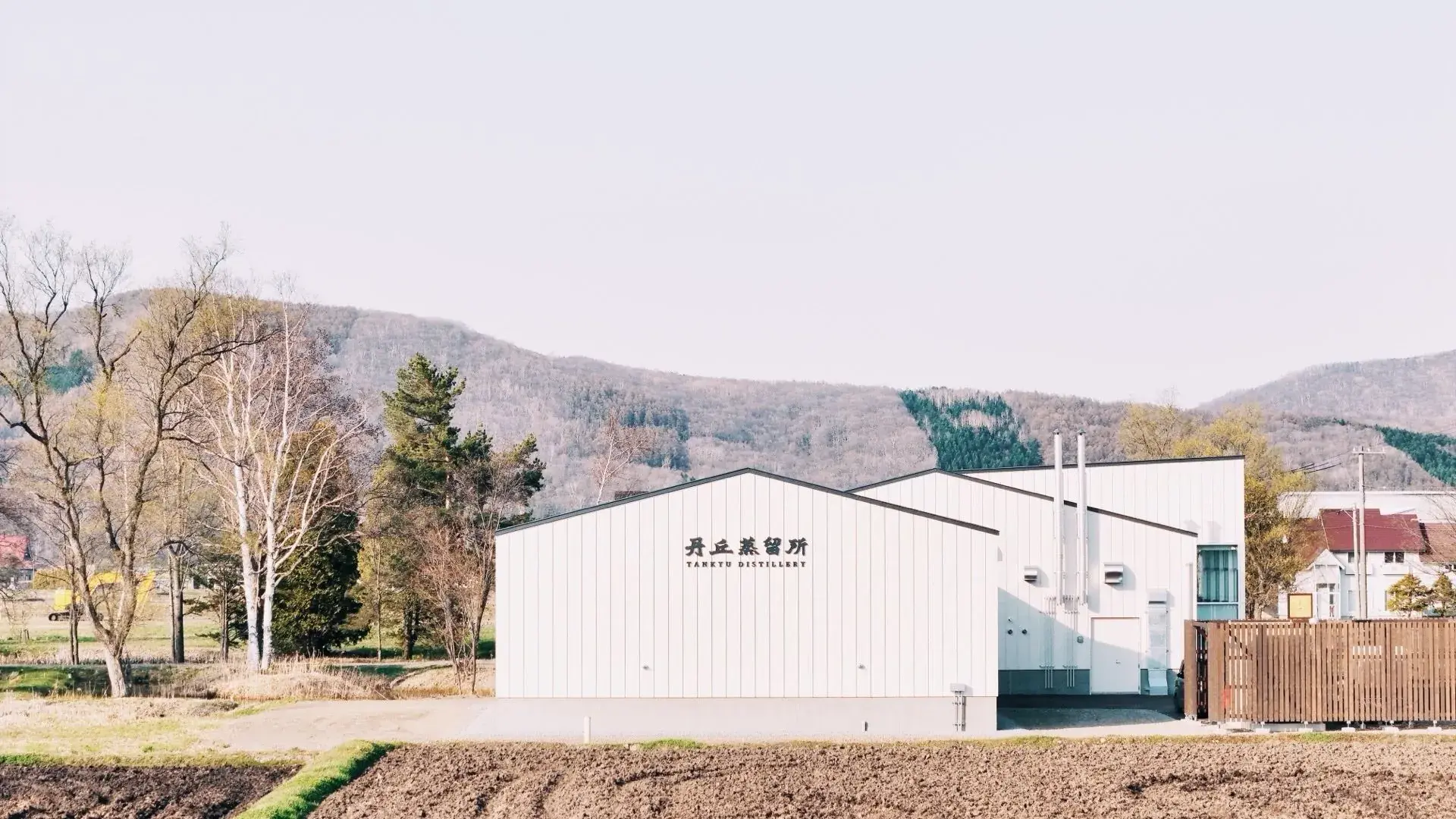 大雪山を背景にした丹丘蒸留所の外観 — 北海道クラフトウイスキー蒸留所