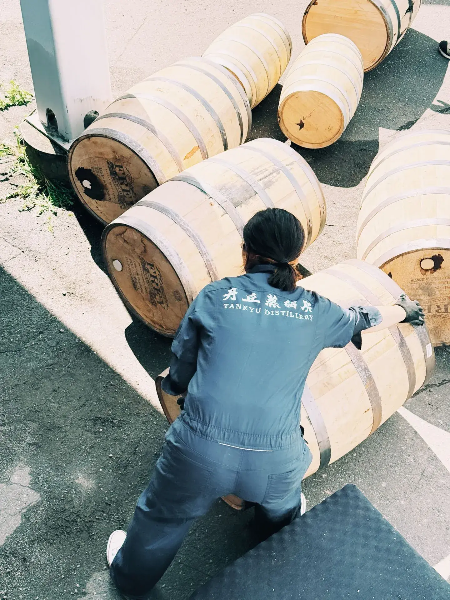 Tankyu Distillery worker rolling oak barrels outdoors